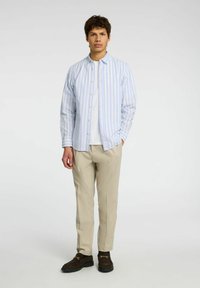 Vaaleansininen ja valkoinen raidoitettu nappipaita, pitkät hihat, yhdistetty beigeihin housuihin ja tummiin kenkiin. Yksinkertainen muotoilu, ei näkyviä kuvioita tai korostuksia.