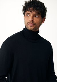 Zwarte coltrui gemaakt van zacht materiaal, met een aansluitende pasvorm, geribbelde kraag en een gladde textuur. Geschikt voor casual gebruik.