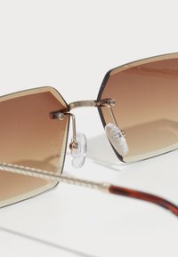 Brune gradient oversized solbriller med vinklete rammer, metallbro og klare nesepads. Skilpaddeskall-templer med teksturerte detaljer.