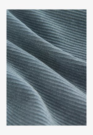 Hallikas soon koos pehme tekstuuriga, millel on õrnad lained ja varjud, rõhutades kudumise mustrit visuaalse sügavuse saavutamiseks.