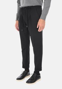 Pantaloni neri con pieghe, vita con cordoncino regolabile e orli arrotolati, abbinati a scarpe nere con suola crema.