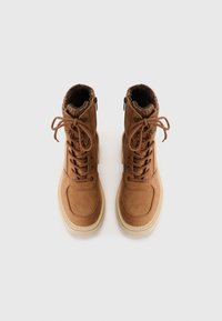 Bottines en daim marron avec lacets, un col rembourré et une semelle en caoutchouc beige. Équipées de zips latéraux et d'accents décoratifs en métal doré.
