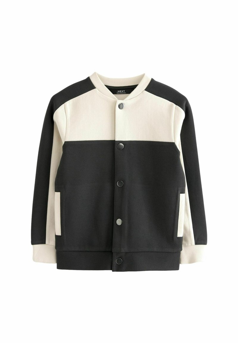 Veste bomber noire et crème avec fermeture à bouton, poignets côtelés et deux poches avant. Présente un design en blocs de couleurs et une texture douce.