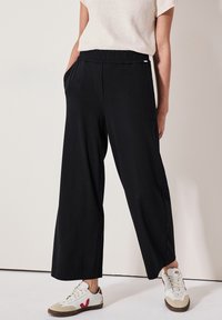 Zwarte wijde pantalon met een elastische tailleband en zijzakken. Gecombineerd met witte sneakers met rode accenten en beige details.