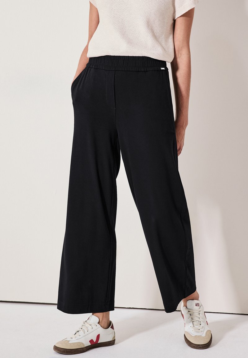 Zwarte wijde pantalon met een elastische tailleband en zijzakken. Gecombineerd met witte sneakers met rode accenten en beige details.