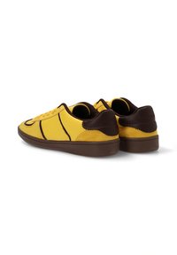 Zapatillas de ante y cuero amarillas con acentos en marrón oscuro, puntera redondeada, cordones planos y suela de goma texturizada.