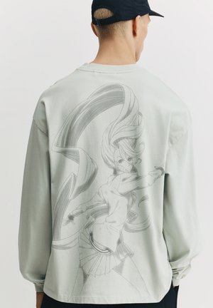 Hellmintgrünes langärmliges Hemd mit einer großen einfarbigen Illustration einer Figur auf der Rückseite, mit detailliertem Haar- und Kleidungsdesign.