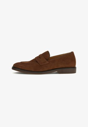 Mocassin homme en daim marron avec une bride et le nom de la marque en relief sur le côté, avec un petit talon et un bout arrondi.