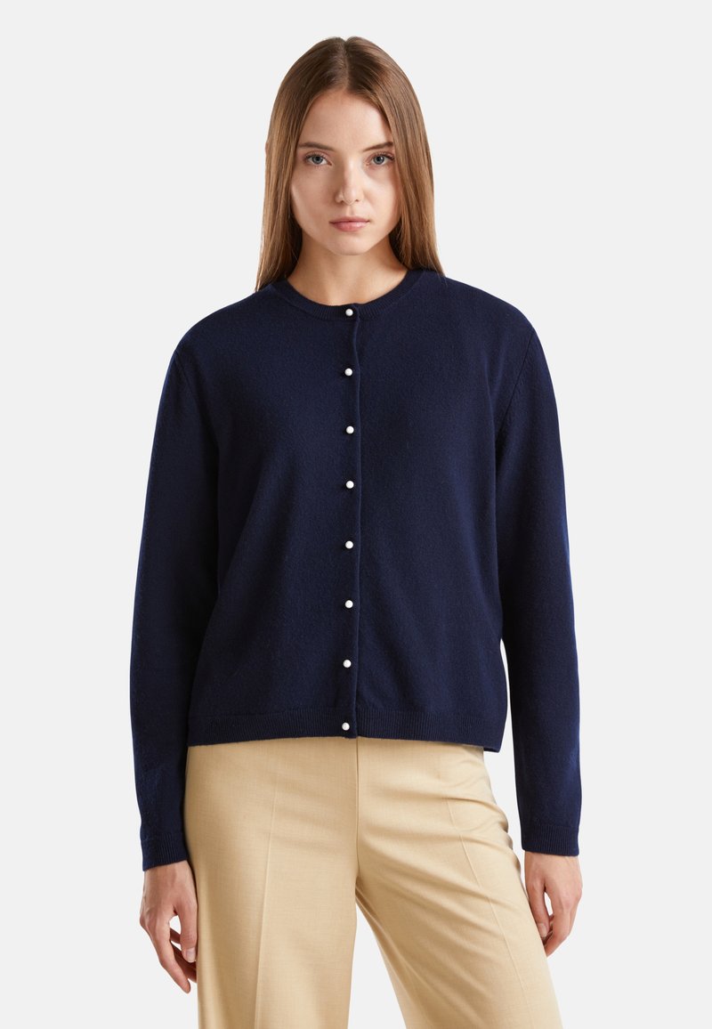 Granatowy kardigan wykonany z miękkiego materiału, z okrągłym dekoltem i zapięciem na guziki z małymi perłowymi akcentami. Długie rękawy i luźny krój.