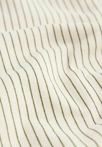 Tissu crème avec de fines rayures noires verticales réparties uniformément sur la surface textile douce et légèrement froissée.