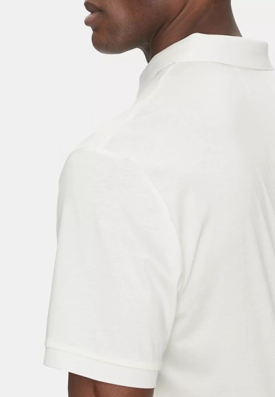 Maglietta polo bianca con una texture liscia, maniche corte e colletto a camicia. Dettagli delle cuciture visibili sulle spalle, vestibilità moderna.