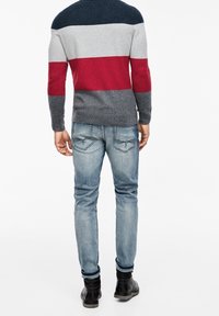 Pull gris avec des rayures rouges et marines, doté d'un col rond, associé à un jean slim bleu clair et des bottines noires.