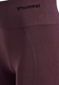 Nahaufnahme von dunkelvioletten Leggings mit hoher Taille und gerippter Textur sowie schwarzem "hummel"-Logo nahe dem Bund.