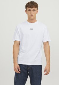 Hvid bomulds t-shirt med rund hals og korte ærmer, med et gråt "JACK & JONES" logo på brystet, parret med mørke jeans.