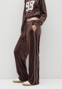 Chándal de terciopelo en marrón oscuro con detalles en blanco, que incluye un top corto con el número 98 y pantalones de corte holgado con bolsillos y cordón.
