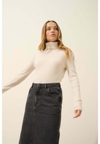 Žebrovaný krémový rolák v kombinaci s džínovou sukní s vysokým pasem, která má zapínání na knoflíky a boční kapsy.