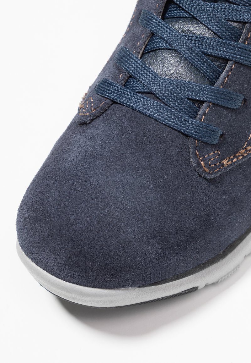 Granatowe zamszowe sneakersy o teksturowanej powierzchni, szarej gumowej podeszwie i ciemnoniebieskich sznurowadłach. Posiadają subtelne przeszycia oraz gładki akcent w okolicy języka.