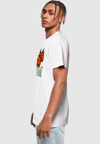 Biely bavlnený tričko s grafickým dizajnom, ktorý zobrazuje oranžové tekvice a zelené akcenty. Krátke rukávy a bežný strih.