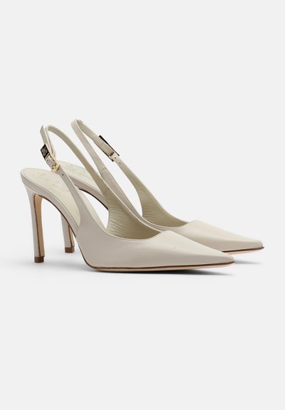 Cremefarbene Leder-Slingback-Pumps mit spitzen Zehen und verstellbaren Schnallen vor weißem Hintergrund.