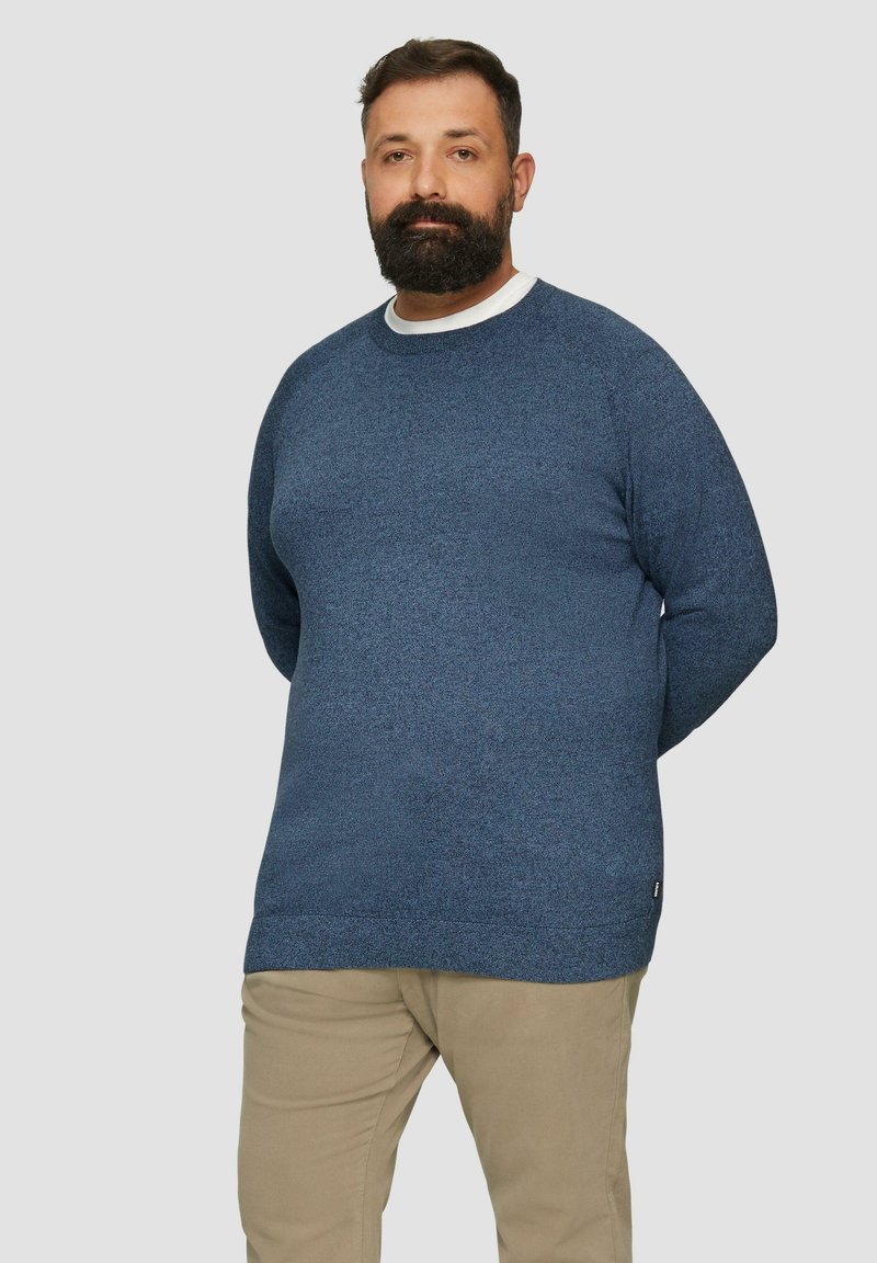 Dunkelblauer Pullover mit strukturiertem Strickdesign, runder Ausschnitt und leicht verlängertem Schnitt. Ergänzt durch beige Hosen.