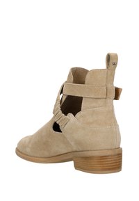 Stivale beige in camoscio con design a taglio aperto, pieghe elastiche e un piccolo tacco impilato. Presenta un piccolo anello sul retro per una facile calzata.