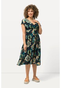 Schwarzes Kleid mit bunten geometrischen Mustern, kurzen Rüschelüfeln und einer taillierten Taille. Tragen mit Plateausandalen.