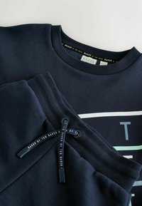 Navyblaues Sweatshirt- und Jogginghosen-Set aus Baumwolle, mit einem gerippten Rundhalsausschnitt, einem Tunnelzugbund und einem weißen Grafikdesign auf dem Sweatshirt.