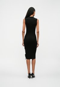 Μαύρο ριπ μίντι φόρεμα με εφαρμοστή σιλουέτα, χωρίς μανίκια και λεπτομέρεια με κορδόνι στο πλάι. Φοριέται με μαύρες ψηλές γόβες.