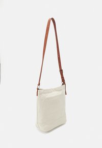 Borsa a spalla in tela di colore bianco sporco, con una tracolla in pelle marrone regolabile, design minimalista e un pannello inferiore cucito per mantenerne la forma.