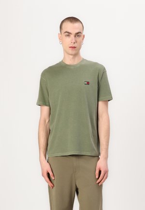 T-shirt in cotone verde oliva con scollo rotondo e maniche corte; presenta un piccolo logo rettangolare sul lato sinistro del petto.