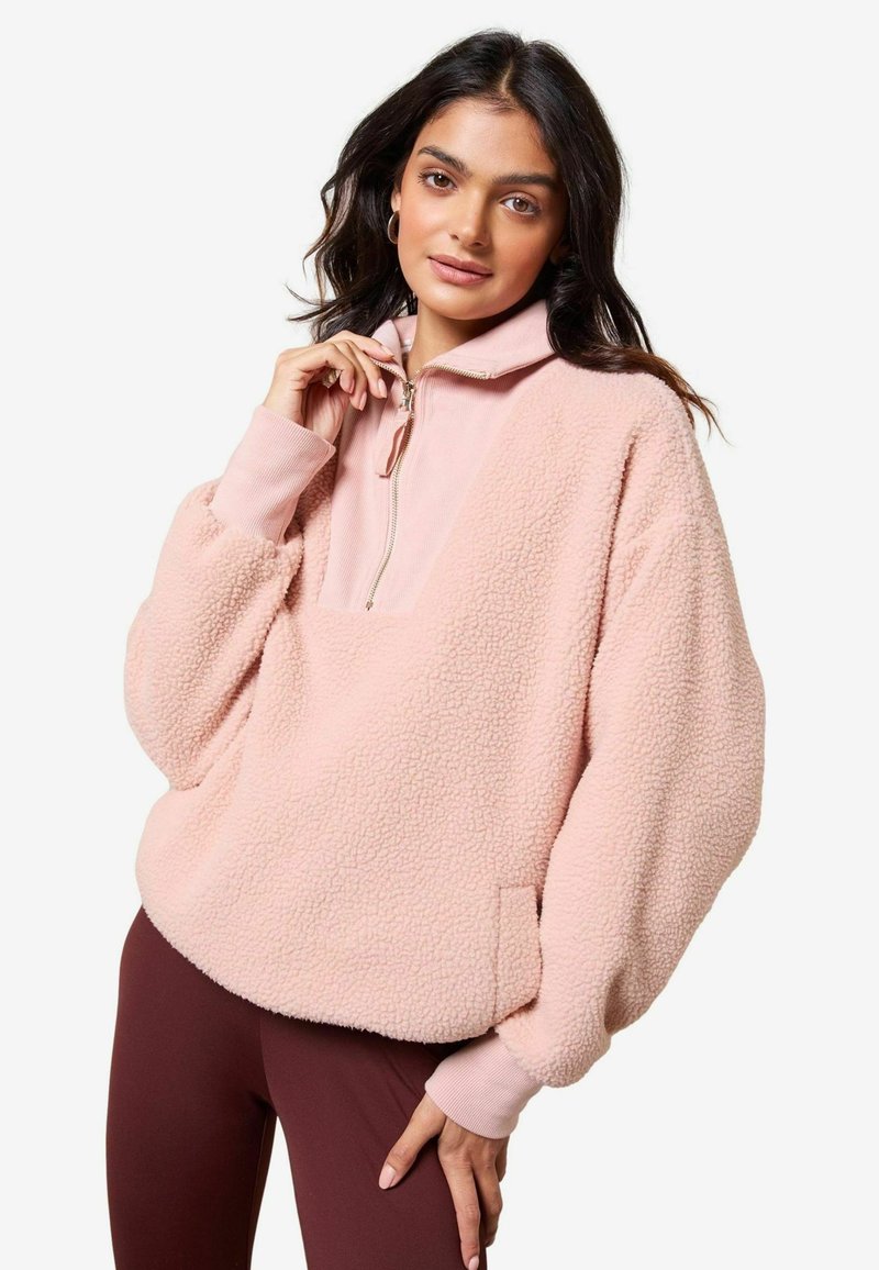 Roosa fliispullover poole tõmblukuga krae, tekstuuriga pind ja suured langetatud õlad. Omab küljetaskuid ja soonikkoes mansette.