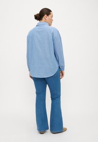 Camisa de manga longa azul riscada com uma bainha curva, combinada com calças de ganga azul à boca de sino. O tecido parece suave com um design clássico.