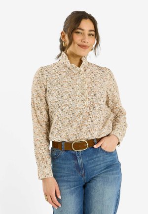 Blusa de flores de manga larga con cuello con volantes, que presenta pequeñas flores multicolores sobre un fondo claro, combinada con vaqueros azules de cintura alta.
