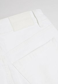 Białe dżinsy z denimu, charakteryzujące się teksturowanym materiałem, tylną kieszenią oraz kwadratową metką wytłoczoną napisem "Diverse Jeans" na pasku.