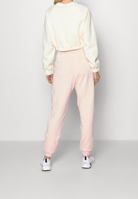 Ljust rosa joggerbyxor med tajta muddar, kombinerade med en krämfärgad sweatshirt med en rynkad midja och raglanärmar.