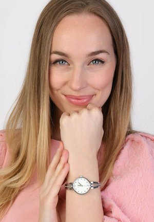 Zilveren polshorloge met een witte wijzerplaat, minimalistische uurmarkeringen en een dubbele armband met kristalaccenten. Gekleed om een hand.