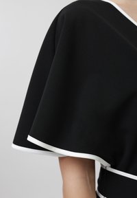 Falda negra con ribete blanco puesta, mostrando un dobladillo de longitud media y parte de la pierna descubierta contra un fondo neutro.