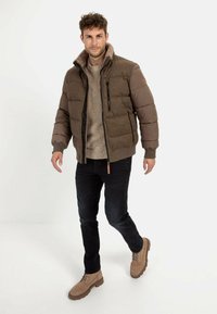Brun polstret jakke med en tekstureret overflade, sorte jeans og tan støvler. Har en høj krave og kontrasterende brune ærmer. Pænt, afslappet look.