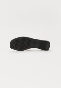 Suela de zapato negra con un patrón texturizado, que presenta un diseño de cuadrícula elevada y un acabado de goma suave. Forma robusta y plana.