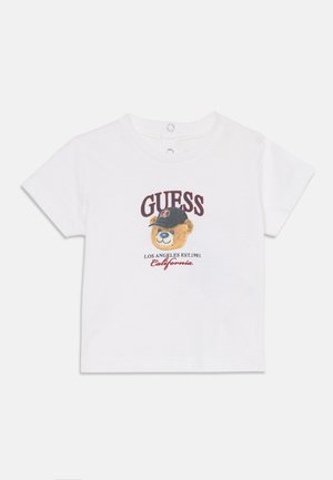 T-shirt blanc à manches courtes pour tout-petit avec un ours portant une casquette noire, texte "GUESS" au-dessus et "Los Angeles Est. 1981 California" en dessous.