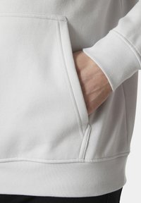 Sudadera gris claro con un bolsillo frontal, puños y dobladillo acanalados. La tela parece suave con una textura lisa y costuras reforzadas.