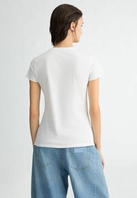 T-shirt en coton blanc à manches courtes, design près du corps. Associé à un pantalon en denim bleu clair avec une étiquette sur la poche arrière.