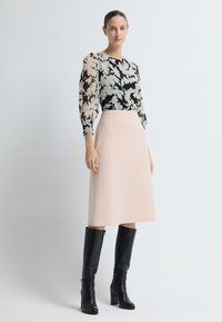 Blusa de manga larga con un patrón floral en negro y crema; falda rosa en corte A; botas de tacón altas negras hasta la rodilla con cremallera.