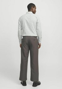 Camisa de botones gris claro con pequeño patrón floral, combinada con pantalones de pierna ancha gris oscuro y zapatos negros.