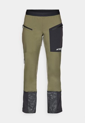 Pantaloni tehnici verzi cu accente negre, buzunare cu fermoar și un model pe partea inferioară a piciorului. Fabricati dintr-un material flexibil și durabil.