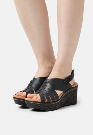 Sandales à bout ouvert noires avec des brides en cuir tressé, une sangle de cheville avec boucle et une semelle compensée texturée. orteils exposés et semelle intérieure brun clair.