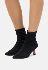 Bottines en daim noir avec un bout pointu et un design loose. Présente un petit talon fin et une texture lisse.