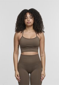 Top corto sportivo marrone con spalline sottili, abbinato a leggings marroni a vita alta. Tessuto liscio, design aderente, senza motivi prominenti.