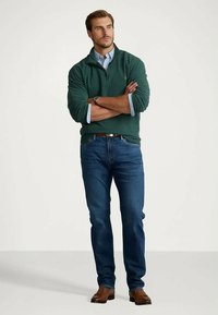 Grønn strikkegenser med glidelås i kragen, lyseblå skjorte med krage under, blå jeans, brunt belte og brune lærsko.