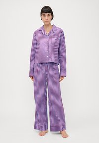 Set de pijamale în dungi violet și alb, cu bluză cu mânecă lungă și nasturi și pantaloni largi. Include un buzunar pe piept și mâneci cu mansete.